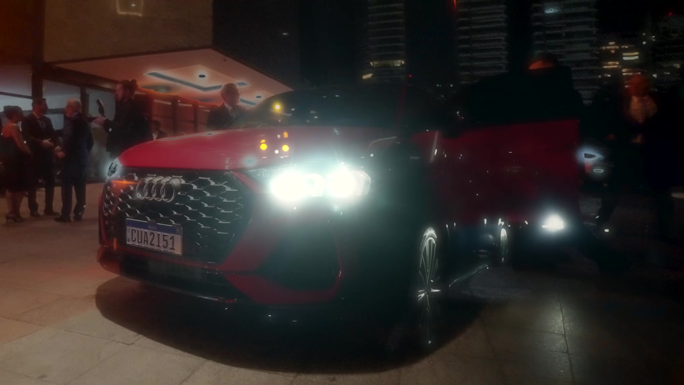 Carro esportivo vermelho com faróis acesos na chegada de um evento à noite